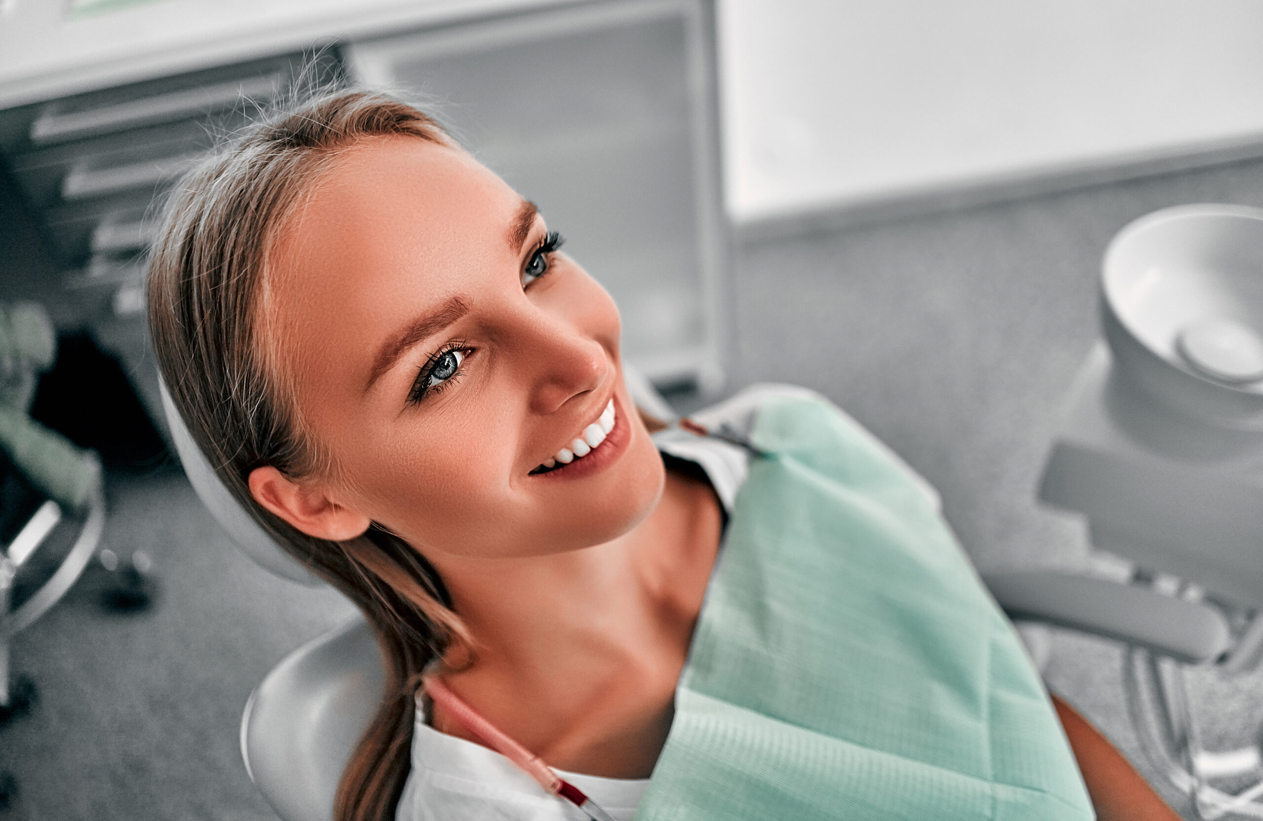 Smiling pretty woman is having her teeth examined by dentist in clinic. Happy young woman sitting in dental chair at dentist office.