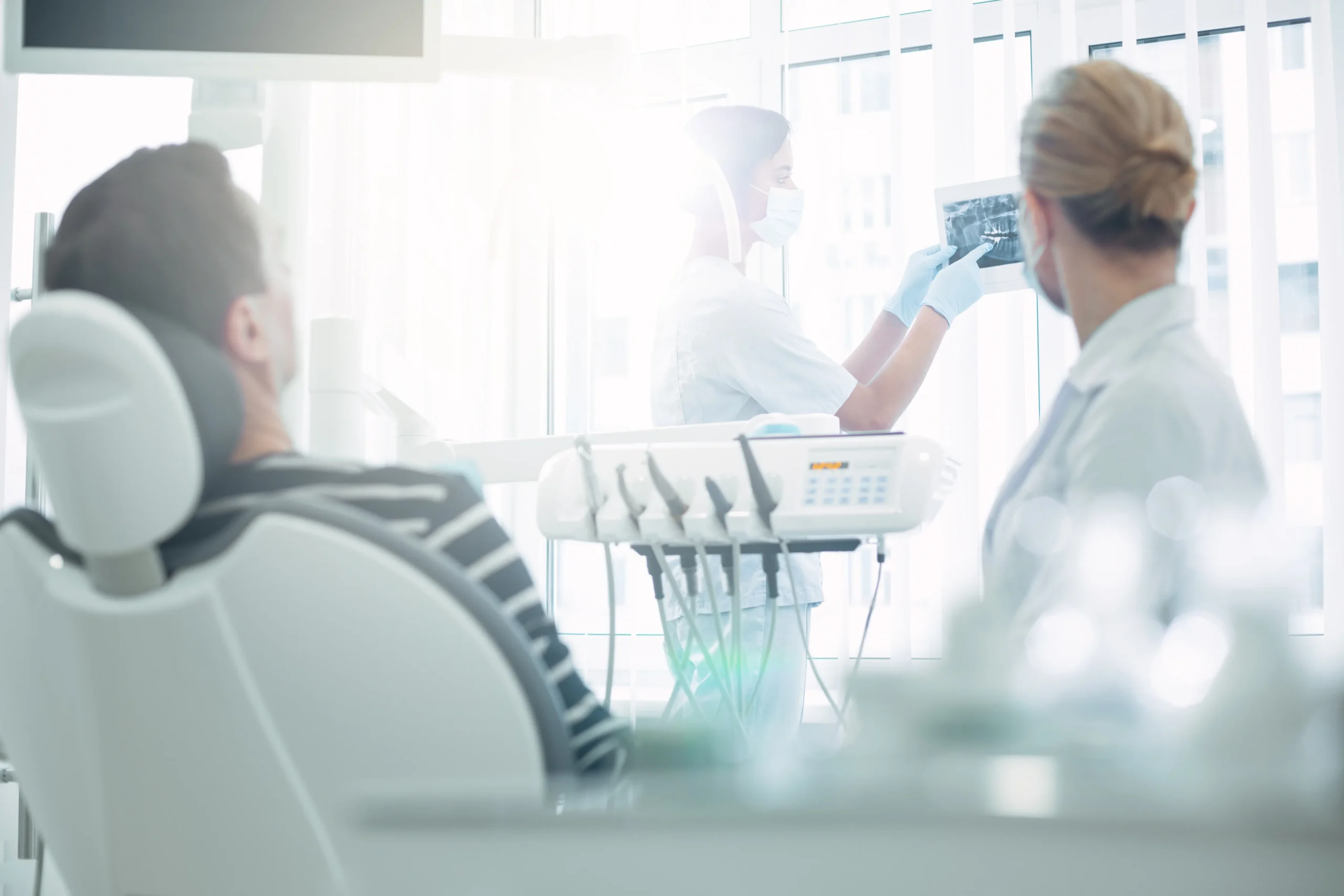 Dark-haired dentist in uniform showing dental X-ray on screen to patient